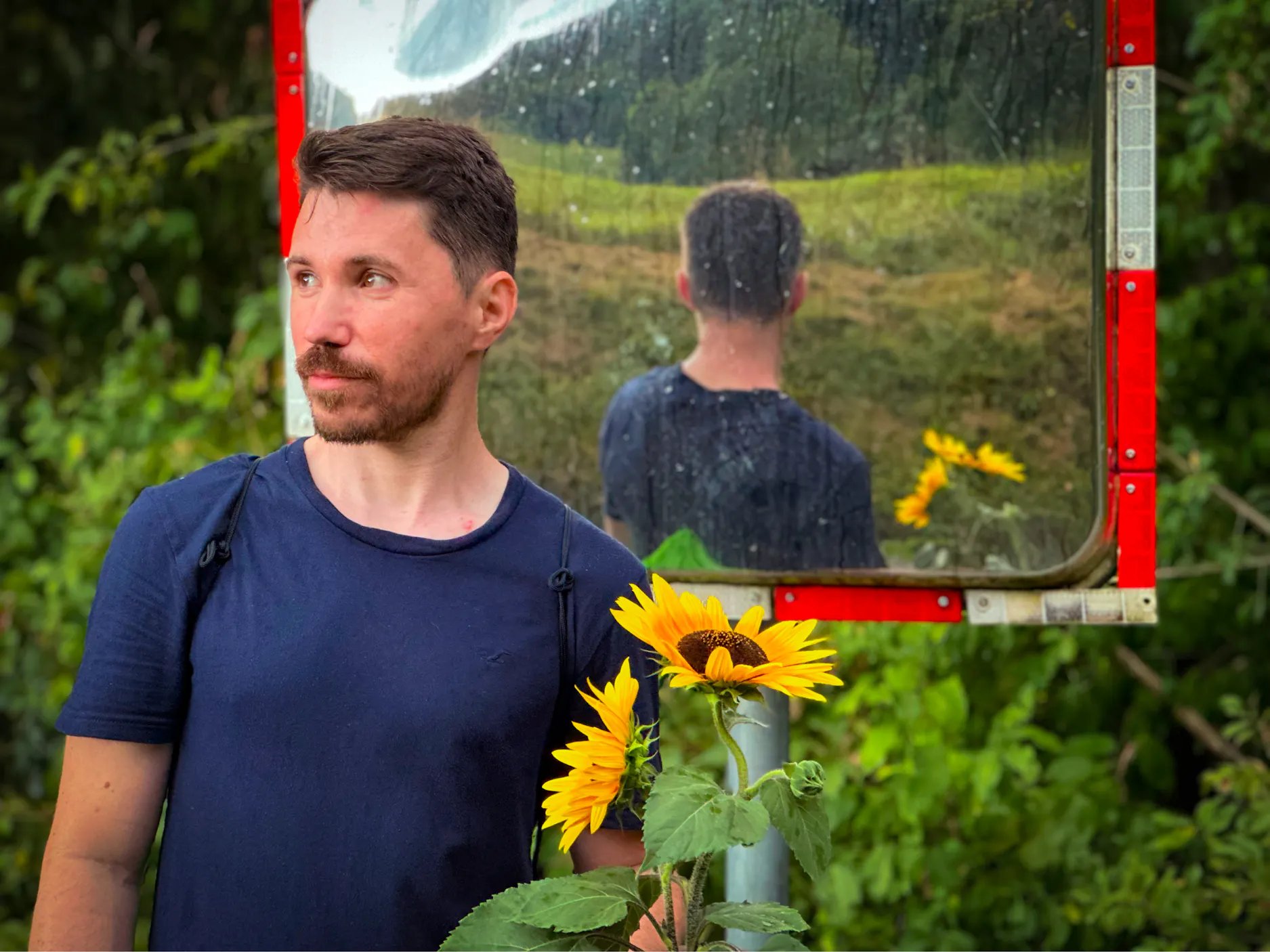 Marko Rop fotografiran pred obcestnim ogledalom s sončnicami v roki.